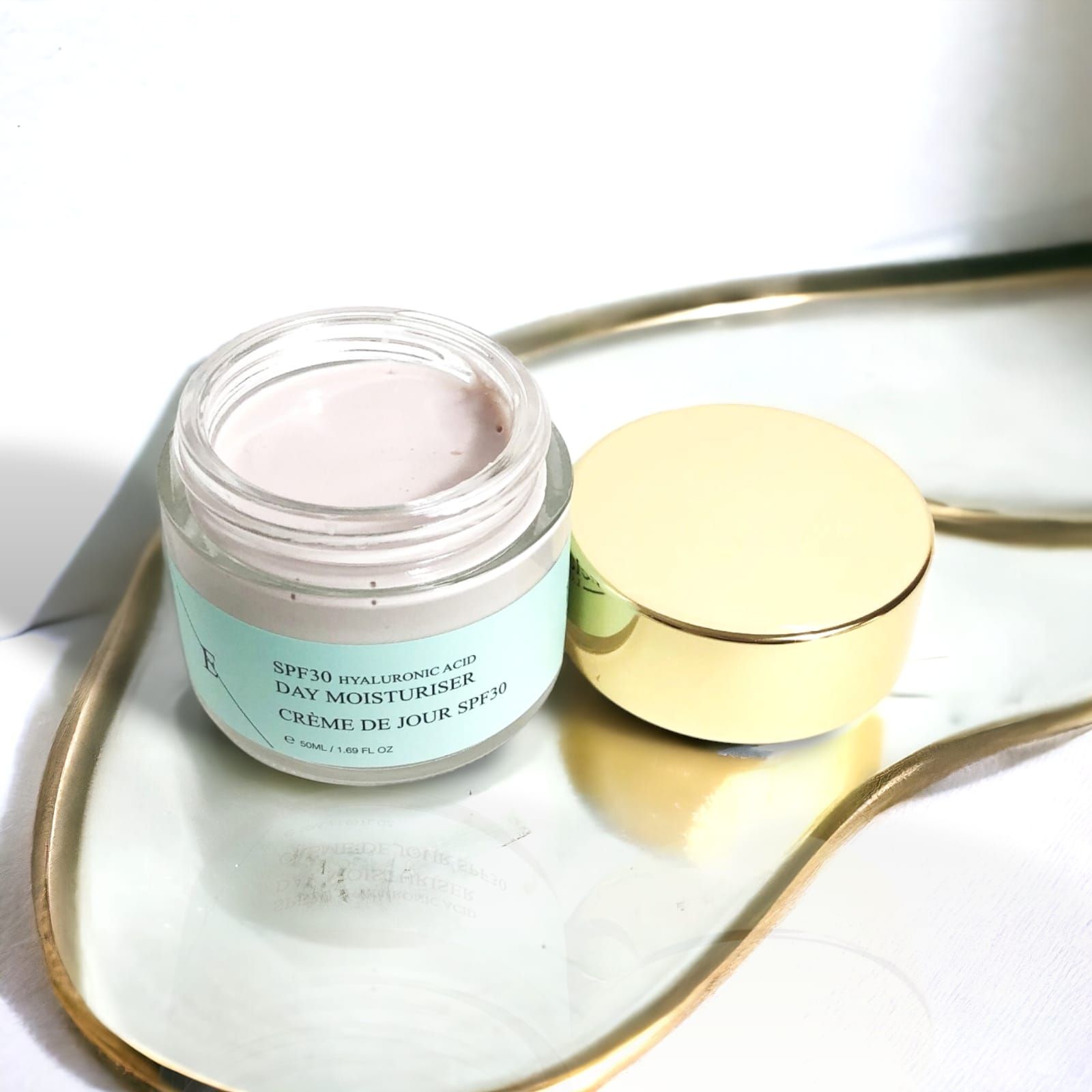 Tagescreme-Tiegel mit goldfarbenem Deckel, geöffnet, auf Tablett. Aufschrift: SPF30 Hyaluronsäure Day Moisturiser Crème de Jour SPF30.