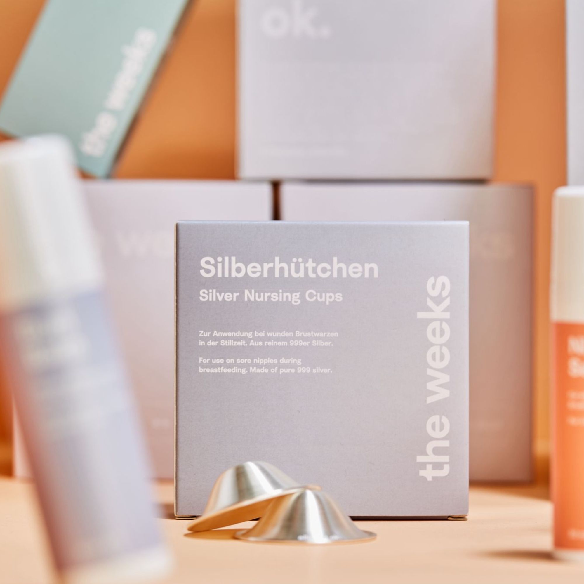 Silberhütchen, zwei silberne Stillhütchen neben Produktverpackung. Verpackung mit Produktname und Logo.