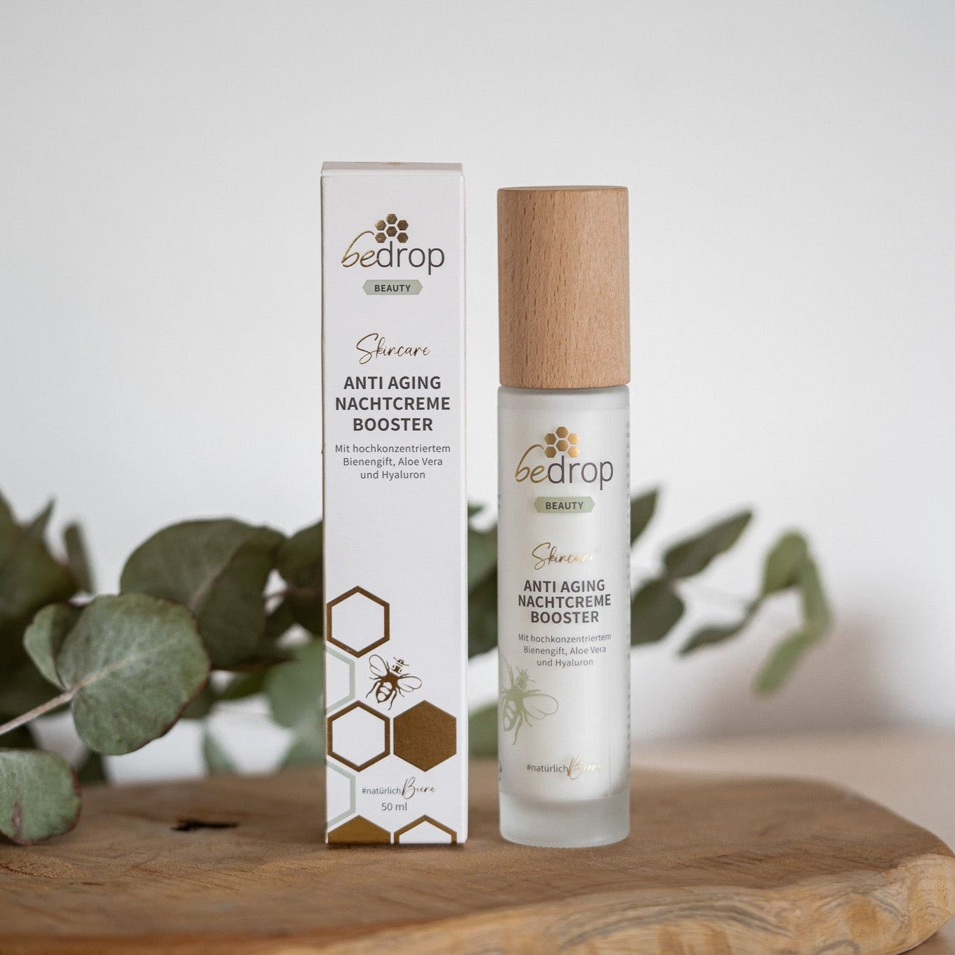 Eine Flasche und Verpackung der Anti-Aging Nachtcreme Booster. Aufschrift: bedrop Beauty, Anti Aging Nachtcreme Booster. Hintergrund: Holzbrett.