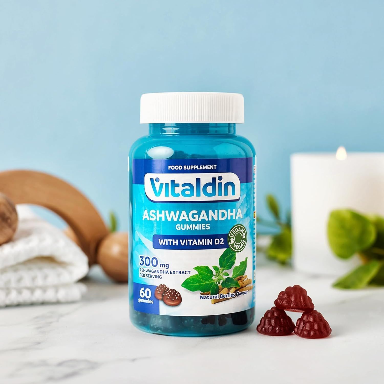 VITALDIN Ashwagandha Gummies Flasche mit 3 Gummibärchen. Auf Tisch mit Kerze und Holzdekoration.