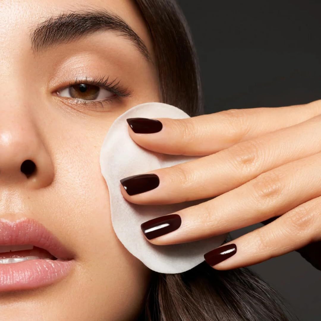 Nahaufnahme einer Frau, die ein Wattepad auf ihr Gesicht aufträgt. Dunkelrote Fingernägel. Hautpflege.