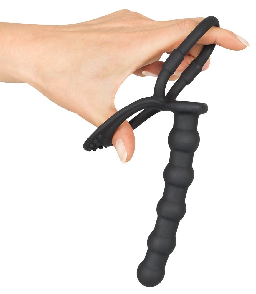 Hand hält schwarzen Penis- und Hodenring mit Analdildo. Ring mit Noppen, Dildo mit geriffelter Oberfläche.
