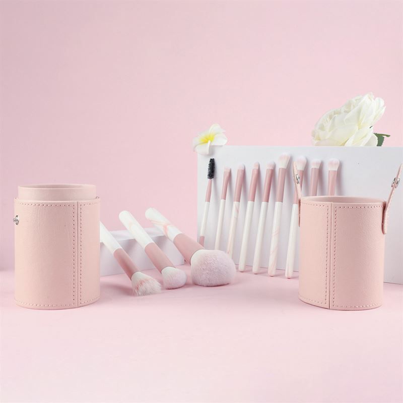 Make-up-Pinsel-Set mit rosa Behältern. Pinsel mit rosa und weißen Griffen. Verschiedene Formen und Größen. Auf rosa Oberfläche platziert.