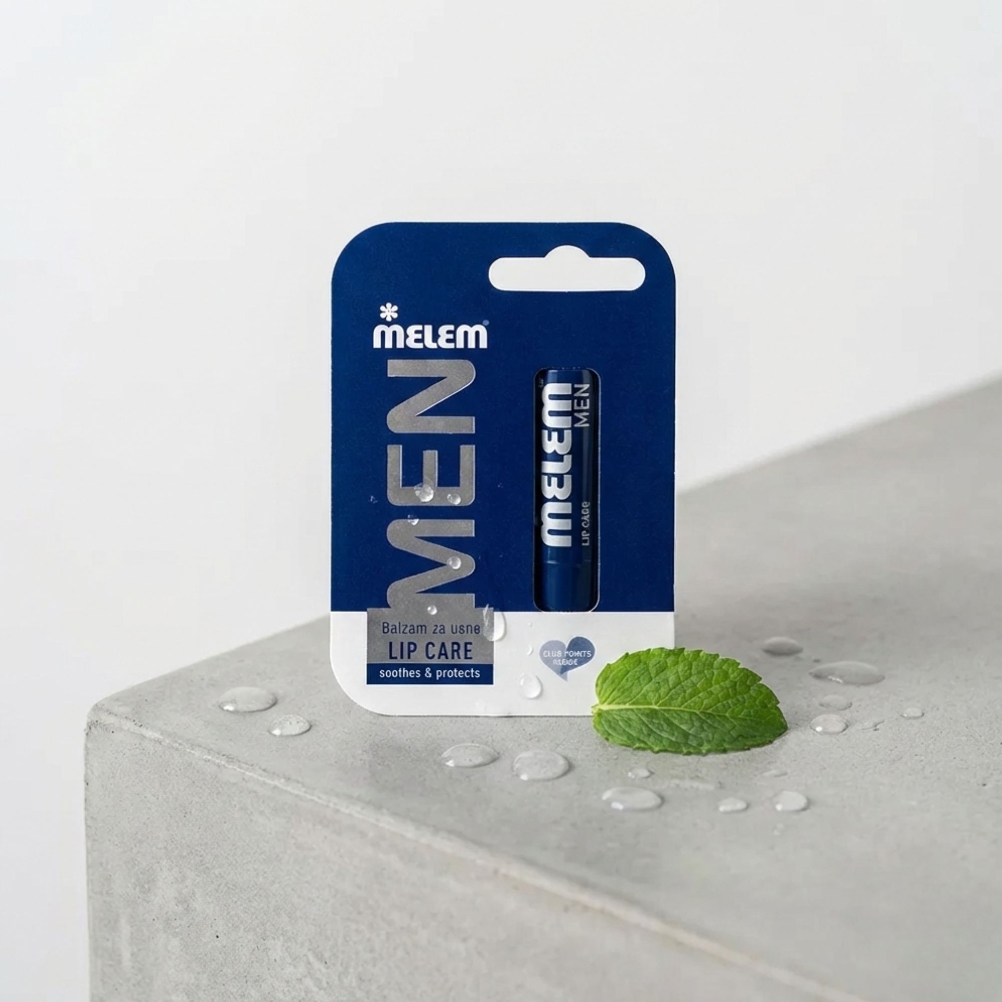 Blauer Lippenbalsam in Verpackung. Aufschrift: MELEM MEN, LIP CARE. Mit Minzblatt und Wassertropfen auf Betonoberfläche.
