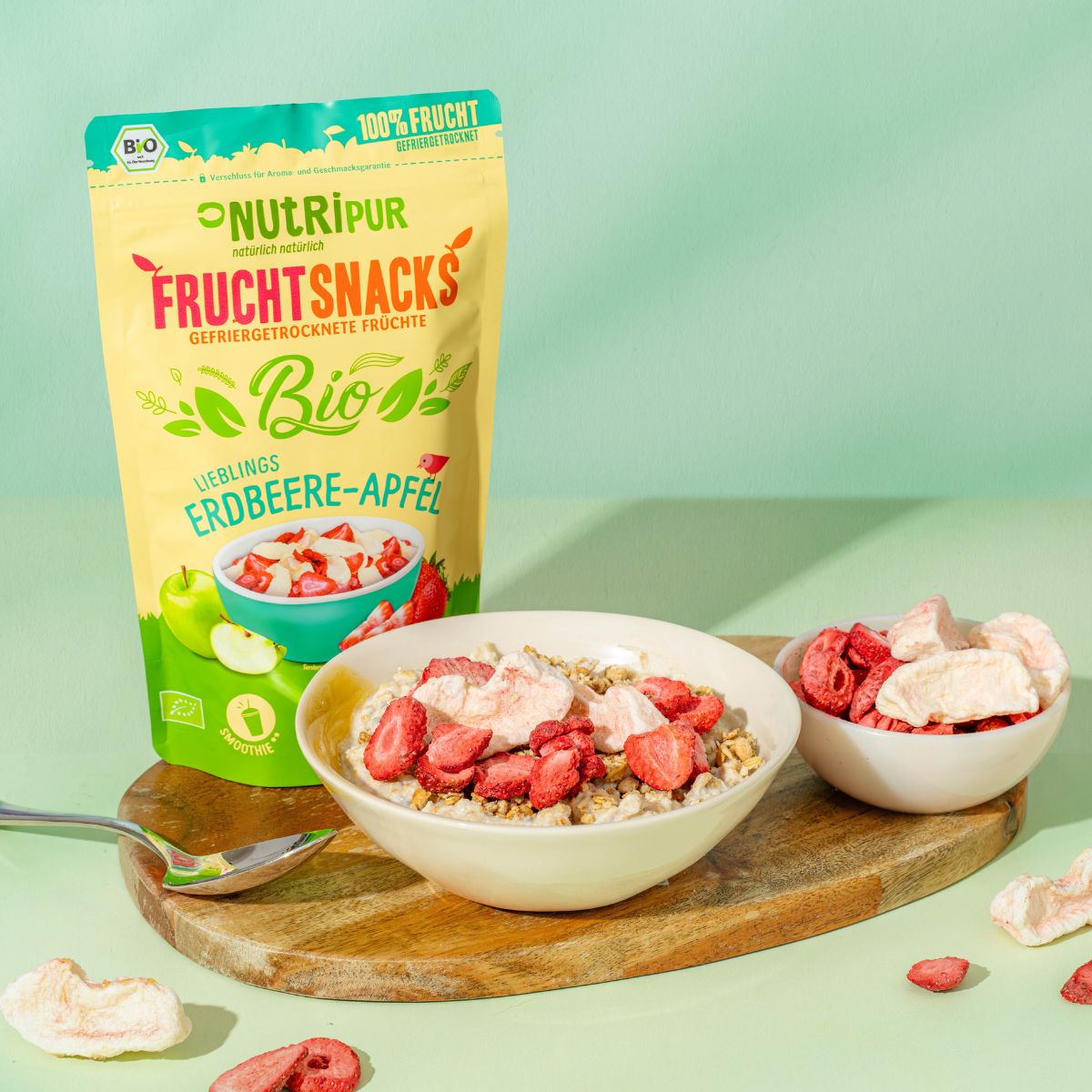 Beutel mit gefriergetrockneten Früchten. Schale mit Müsli und Früchten. Schale mit gefriergetrockneten Früchten. Löffel auf Holzbrett.