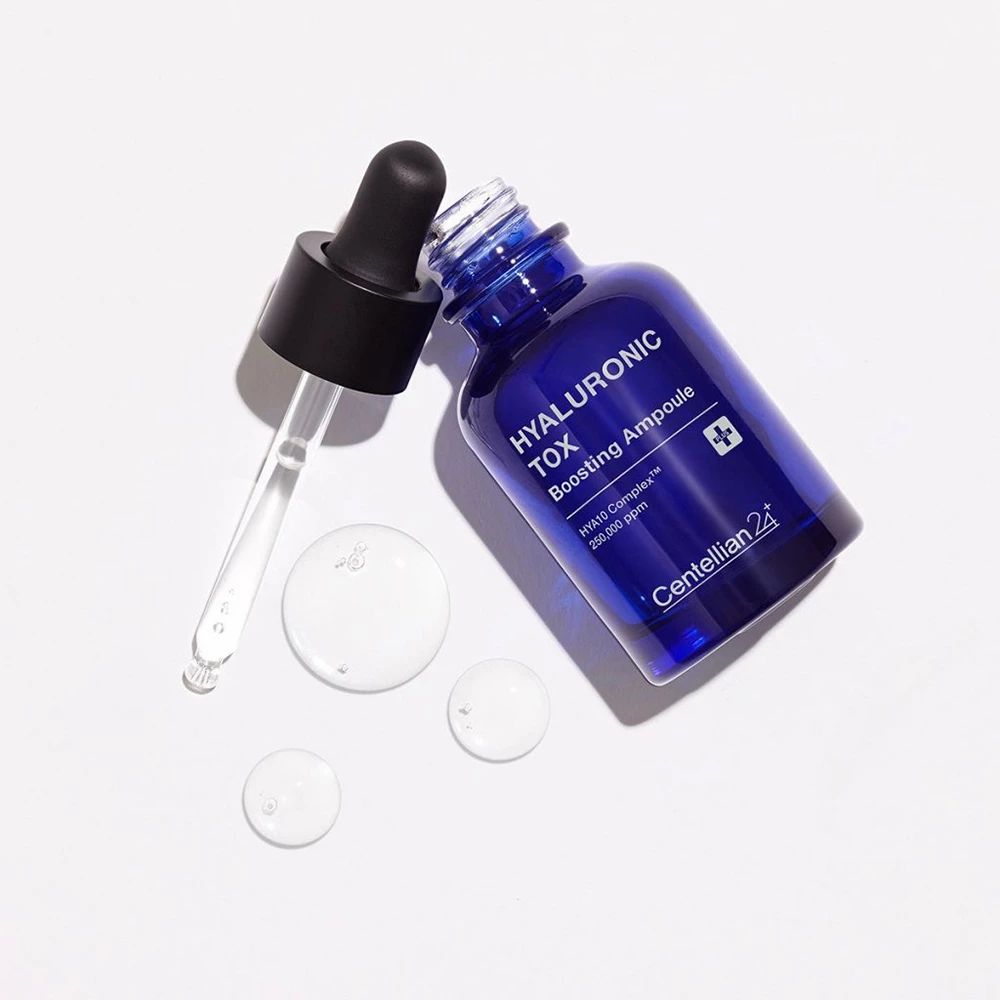 Blaue Flasche mit schwarzem Deckel und Pipette. Daneben liegen drei transparente Tropfen. Aufschrift: HYALURONIC TOX.