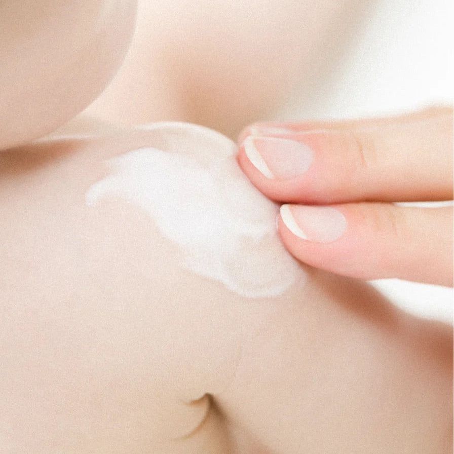 Nahaufnahme: Finger tragen weiße Creme auf die zarte Haut eines Babys auf.