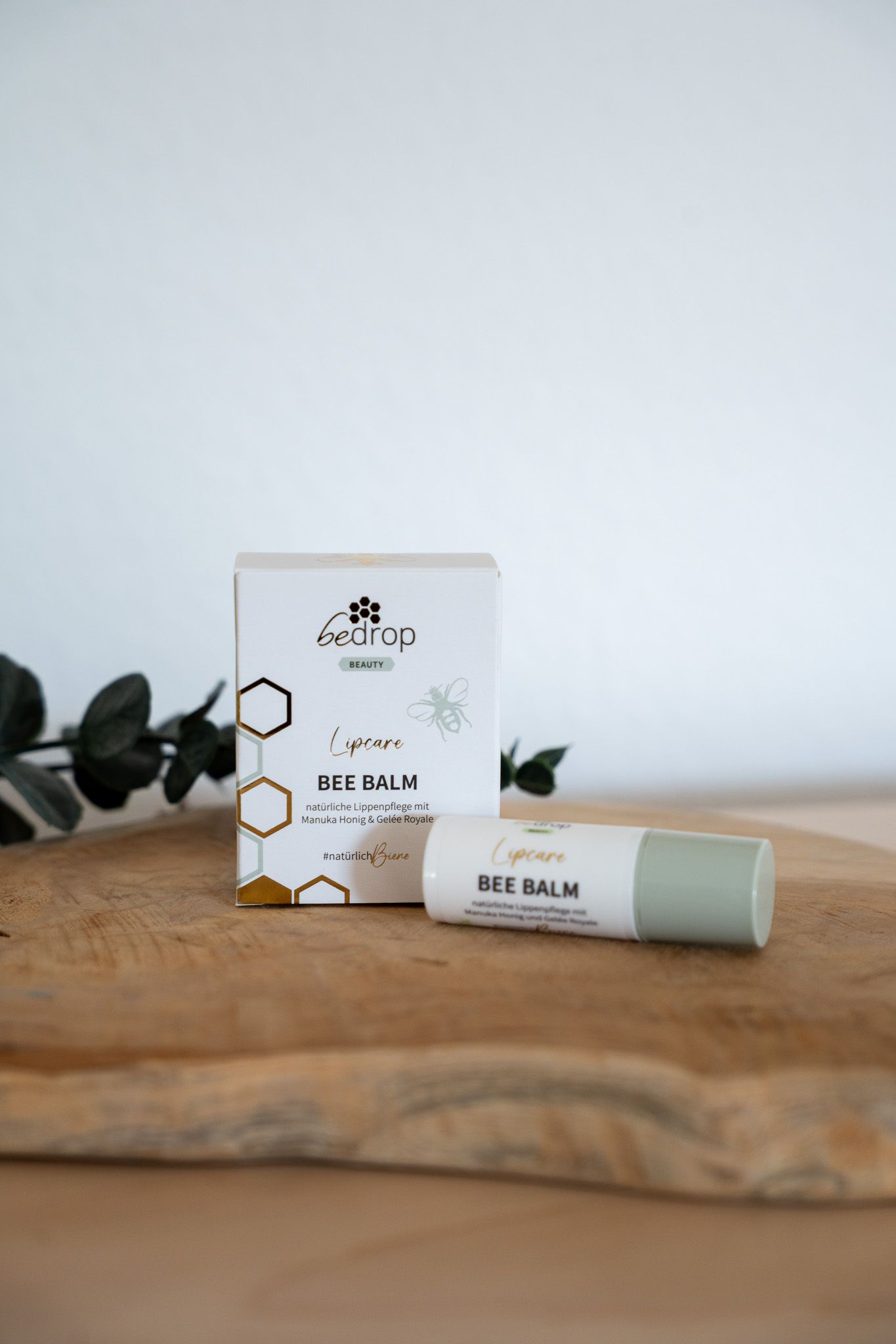 Lippenbalsam und Verpackung auf Holzbrett. Aufschrift: BEE BALM, Lipcare, bedrop. Verpackung mit Bienen-Logo.