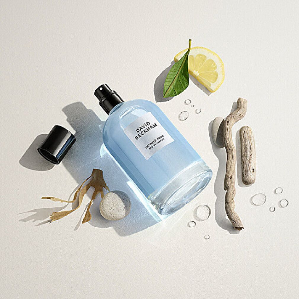 Glasflakon mit blauer Flüssigkeit, schwarzem Verschluss. Text: DAVID BECKHAM, INFINITE AQUA, Eau de Parfum. Dekoration: Zitrone, Holz, Algen.