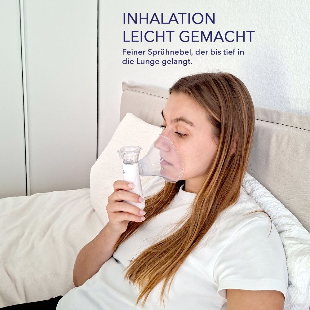 Frau mit Inhalationsgerät und Maske. Gerät weiß, Maske transparent. Frau sitzt auf Bett, hält Gerät. Text: Inhalation leicht gemacht.