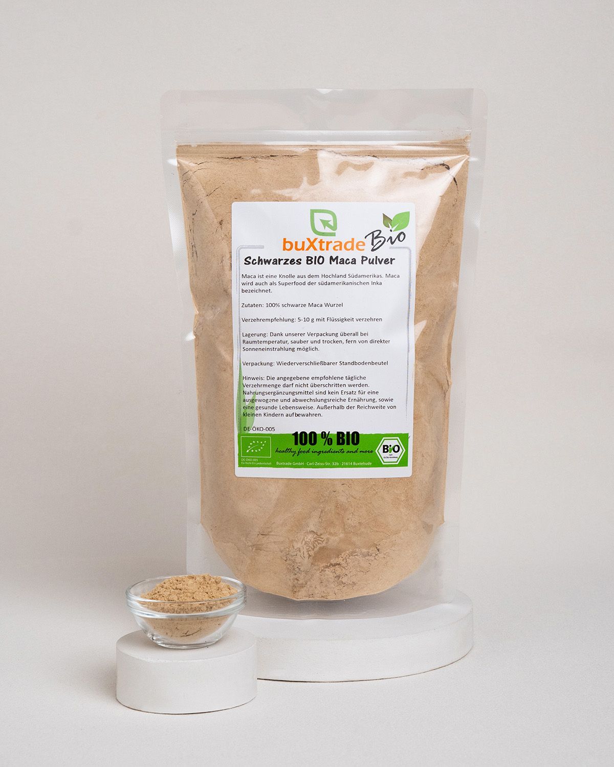 Transparenter Beutel mit buXtrade Bio Maca Pulver schwarz. Kleines Glas mit Pulver daneben. Bio-Siegel.