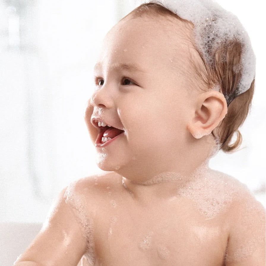 Lächelndes Baby mit Schaum auf dem Kopf in der Badewanne.