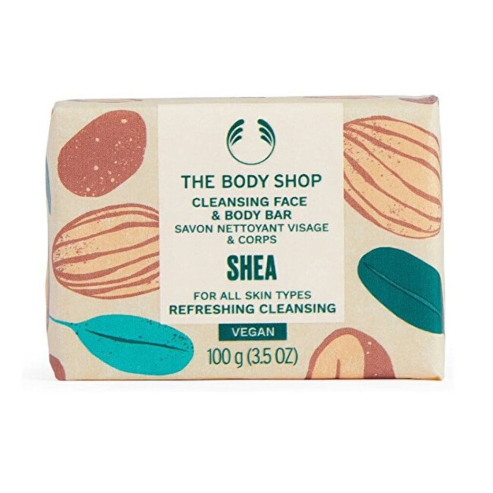 Verpackte Seife. Aufschrift: The Body Shop, Cleansing Face & Body Bar, Shea, Vegan. 100 g. Mit braunen und grünen Mustern.