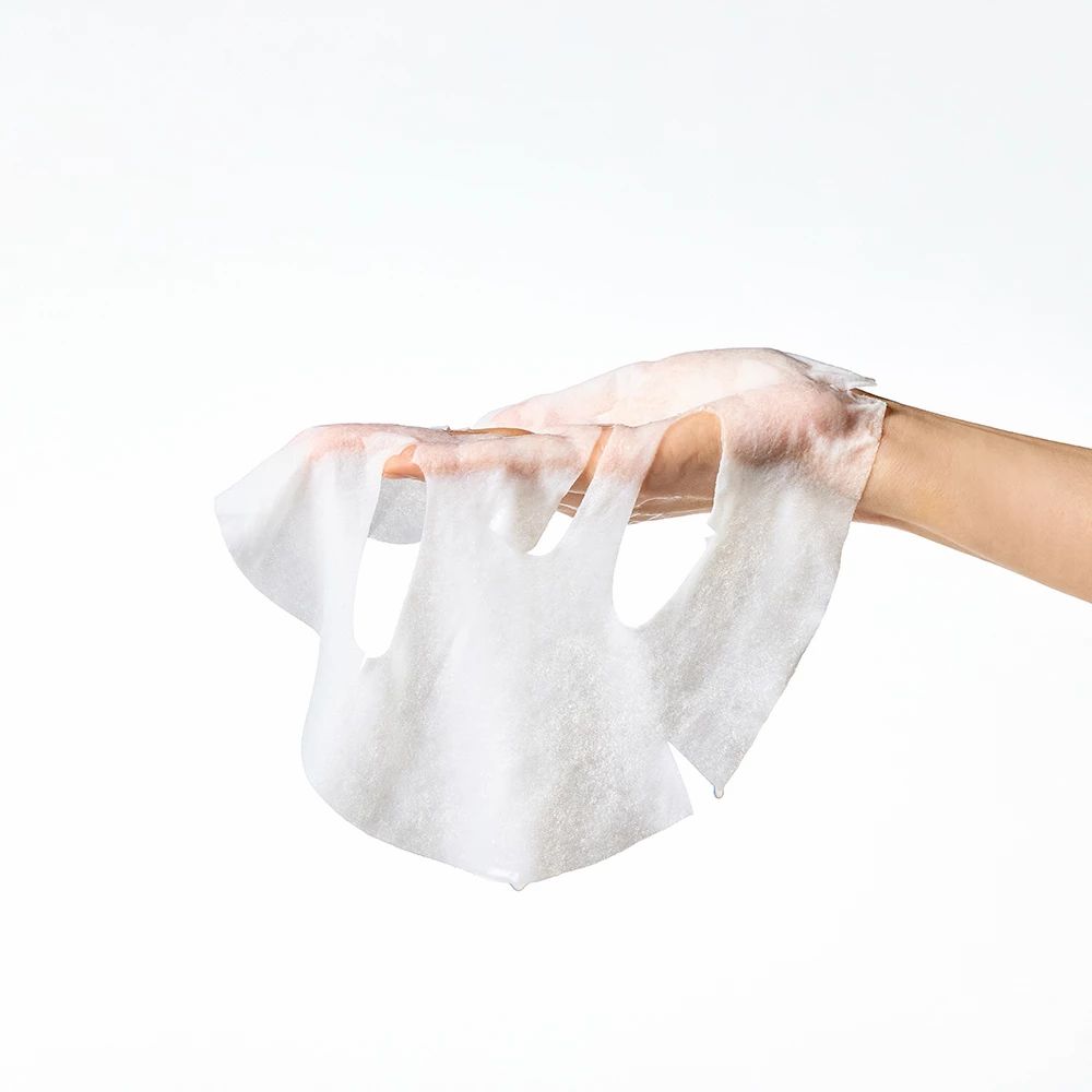 Hände halten eine weiße Gesichtsmaske. Aussparungen für Augen, Nase und Mund. Hintergrund weiß.