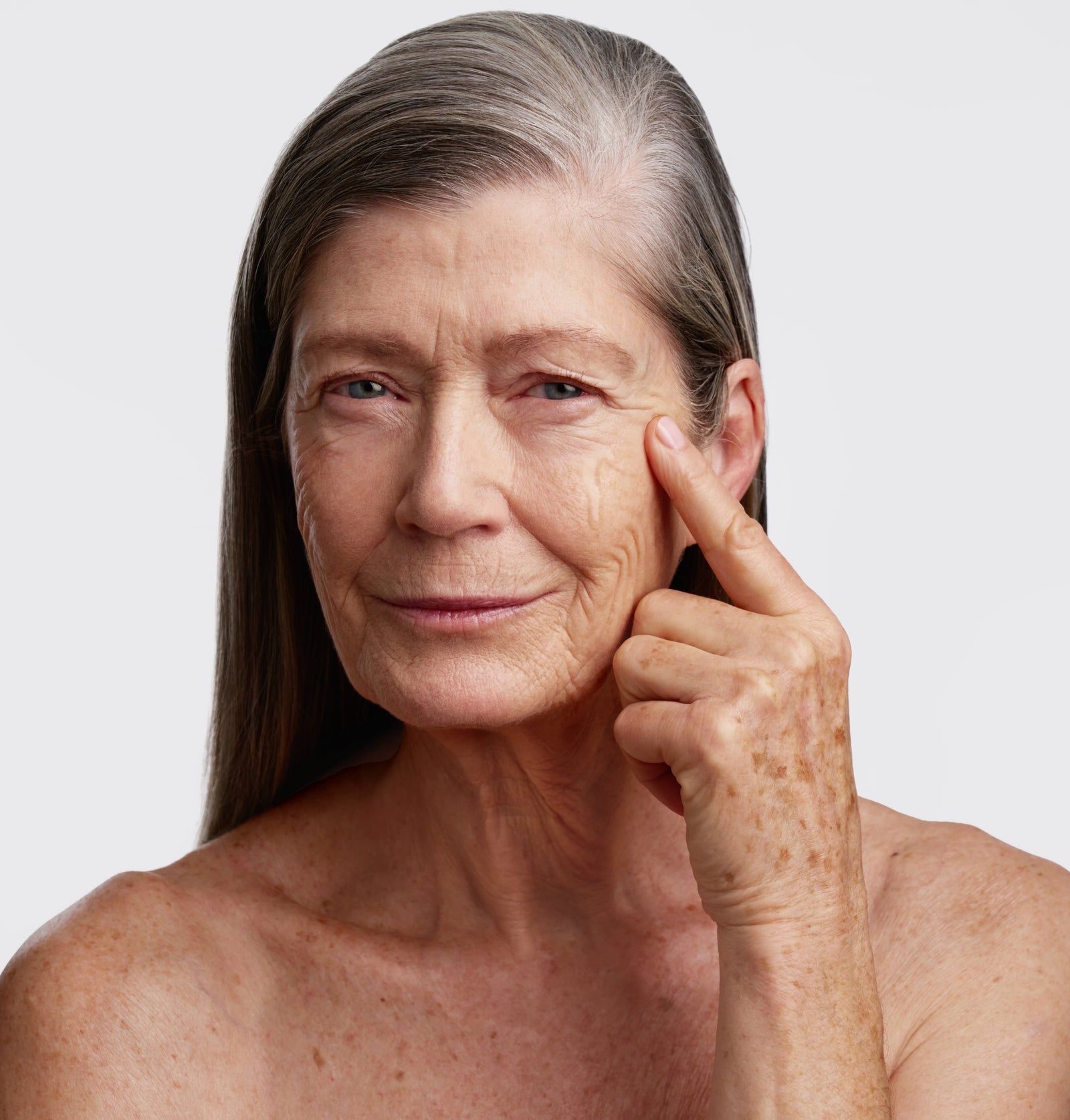 Ältere Frau mit grauen Haaren, berührt ihre Haut unter dem Auge. Haut mit Sommersprossen.
