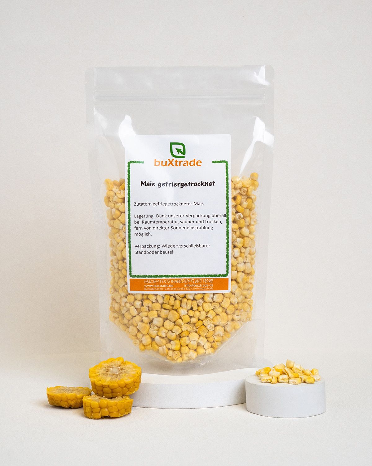 Verpackung mit gefriergetrocknetem Mais, daneben Maiskolbenscheiben und Maiskörner in Schale. Produktpräsentation.