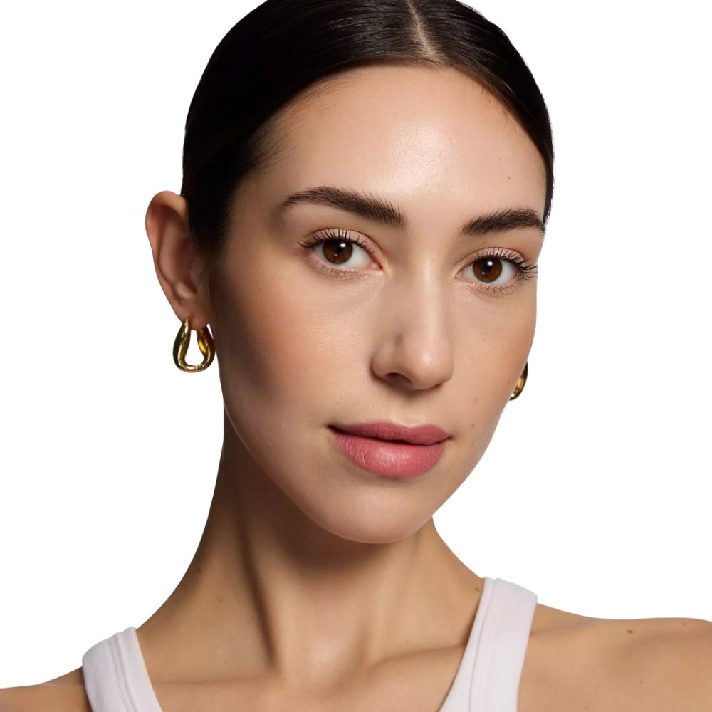 Porträt einer Frau mit Lippenstift. Goldene Ohrringe. Weißes Oberteil. Heller Hintergrund.