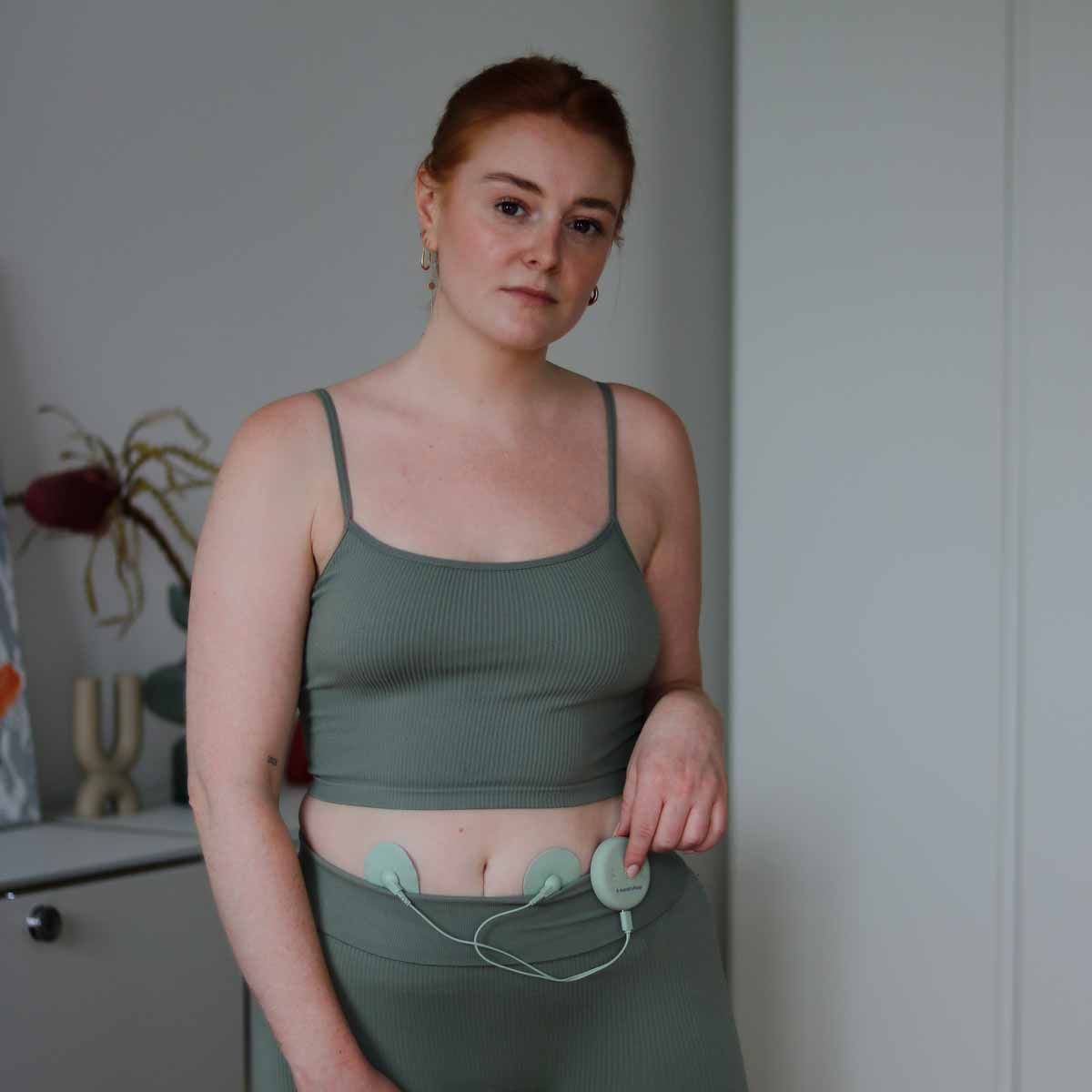 Frau mit zwei grünen Pads am Unterbauch, verbunden mit einem Steuergerät.