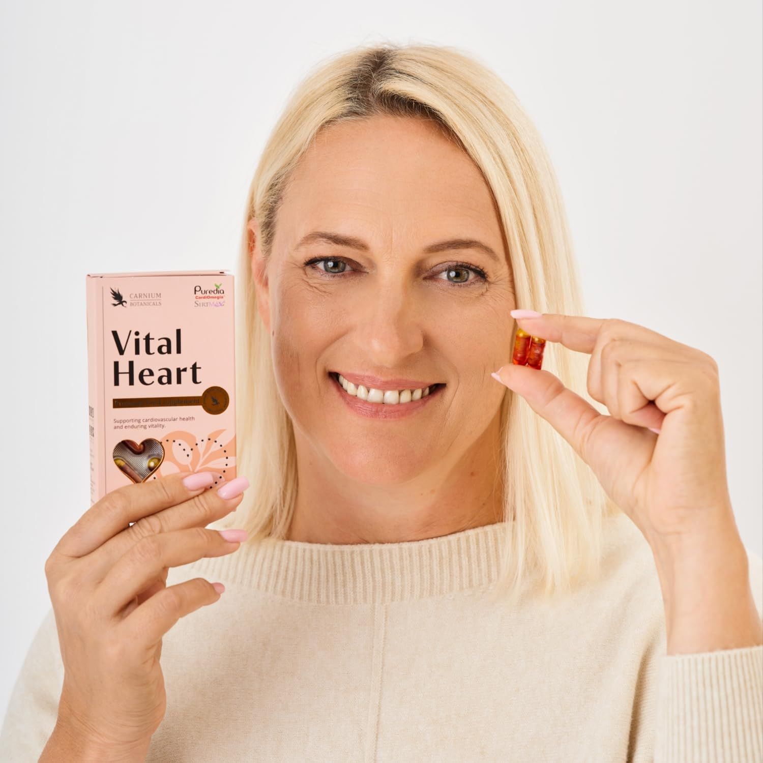 Frau hält eine Kapsel und eine rosa Schachtel "Vital Heart" in der Hand.