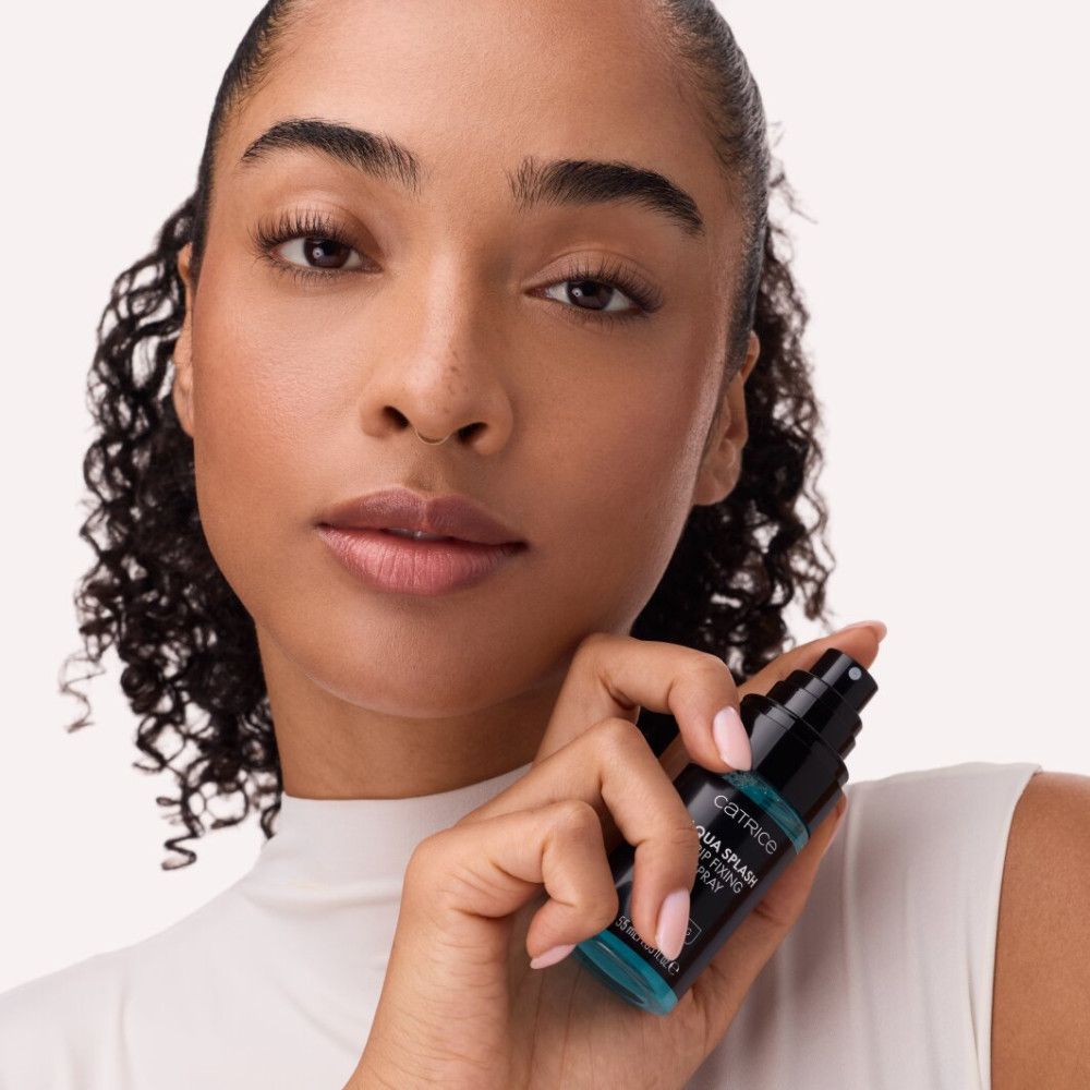 Frau hält eine schwarze Sprühflasche mit blauem Inhalt. Aufschrift: Catrice, Aqua Splash Grip Fixing Spray. Hydratisierend.