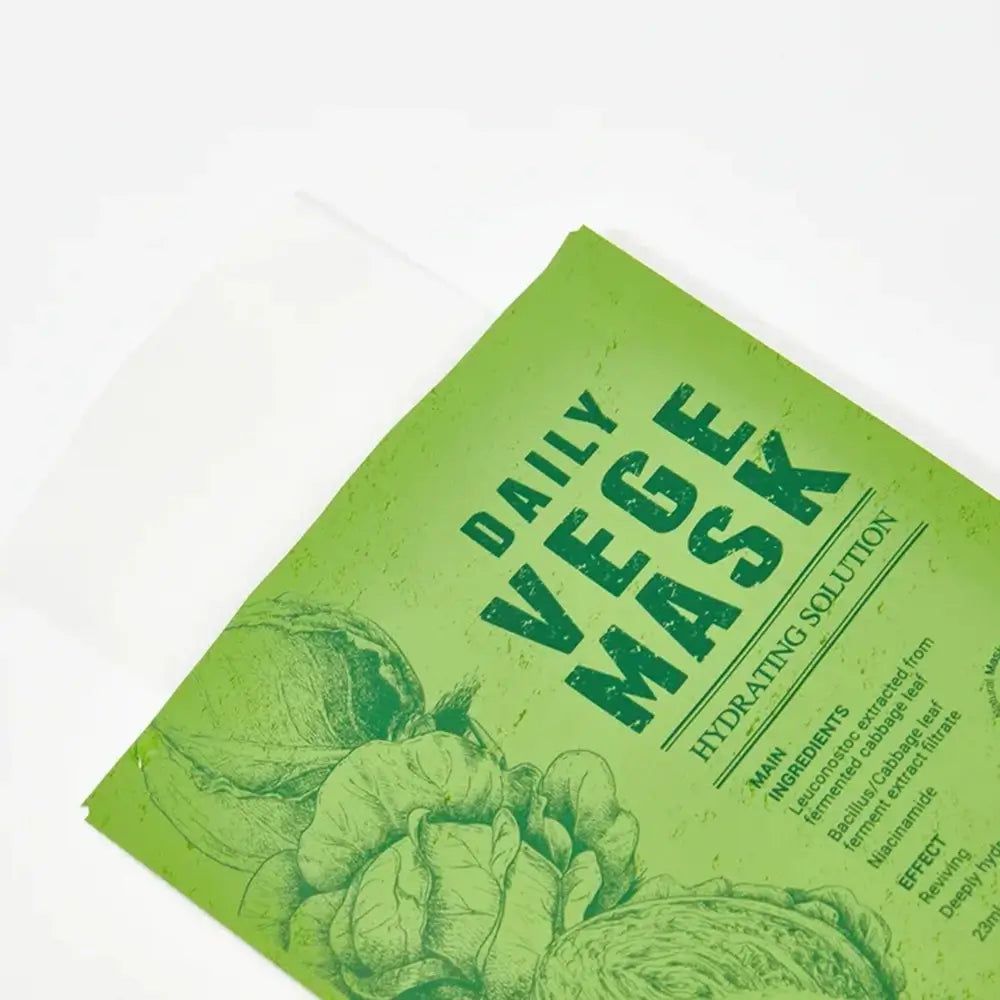 Grüne Gesichtsmaske mit Aufdruck "DAILY VEGE MASK". Hauptbestandteile und Inhaltsstoffe sind aufgedruckt. Aufdruck von Gemüse-Illustrationen.