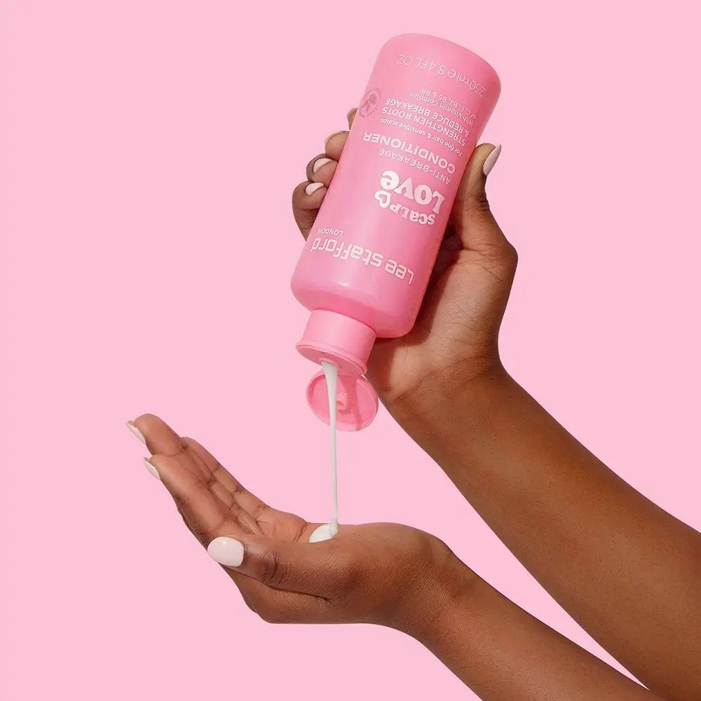 Eine Hand hält eine rosa Flasche Conditioner, aus der weiße Flüssigkeit in die andere Hand fließt.
