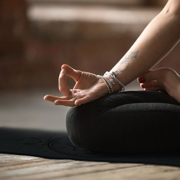 Nahaufnahme einer Hand in der Lotus-Position auf einer Yogamatte. Die Matte ist dunkelgrau.