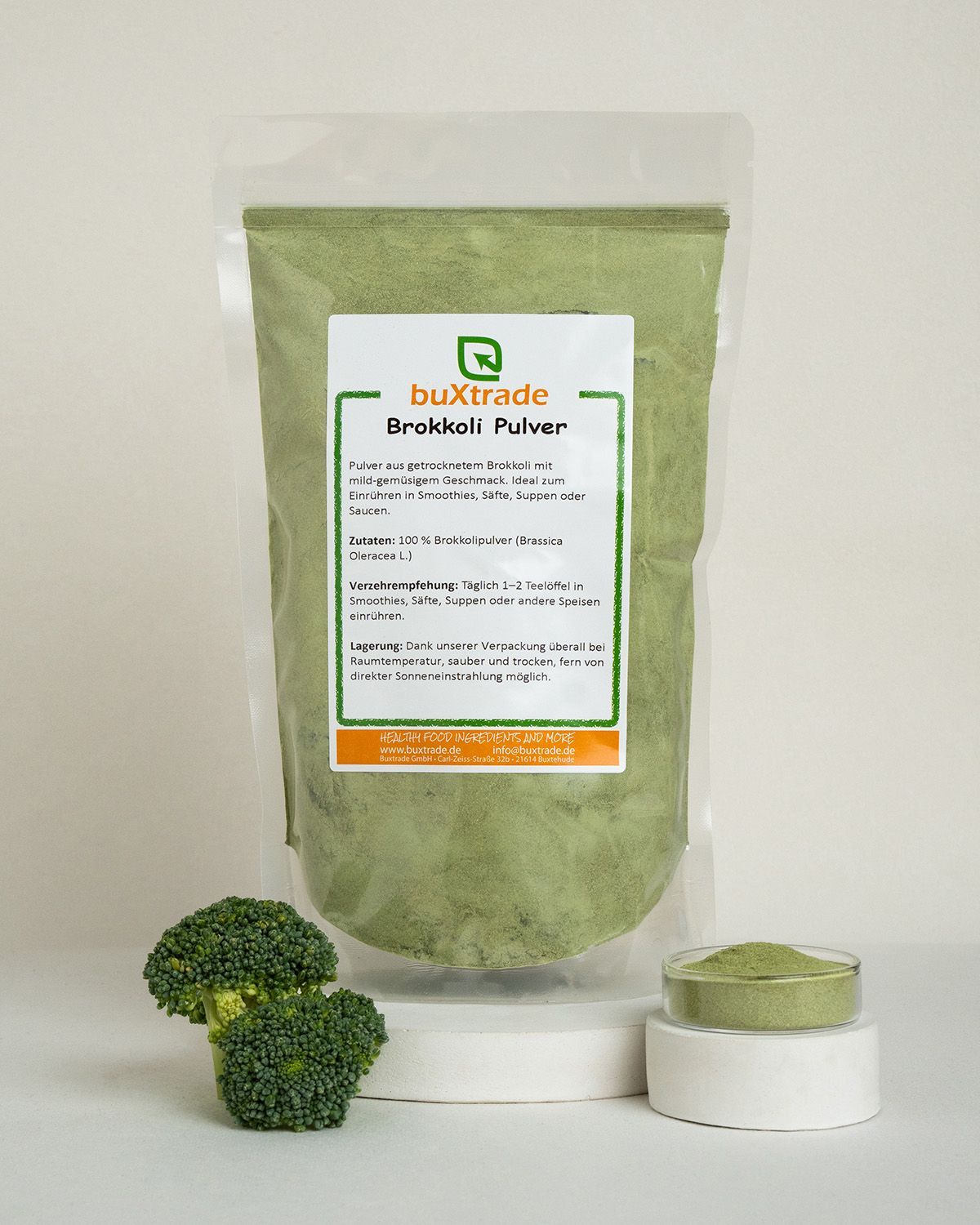 Verpackung mit buXtrade Brokkoli Pulver, daneben frische Brokkoliröschen und Pulver.