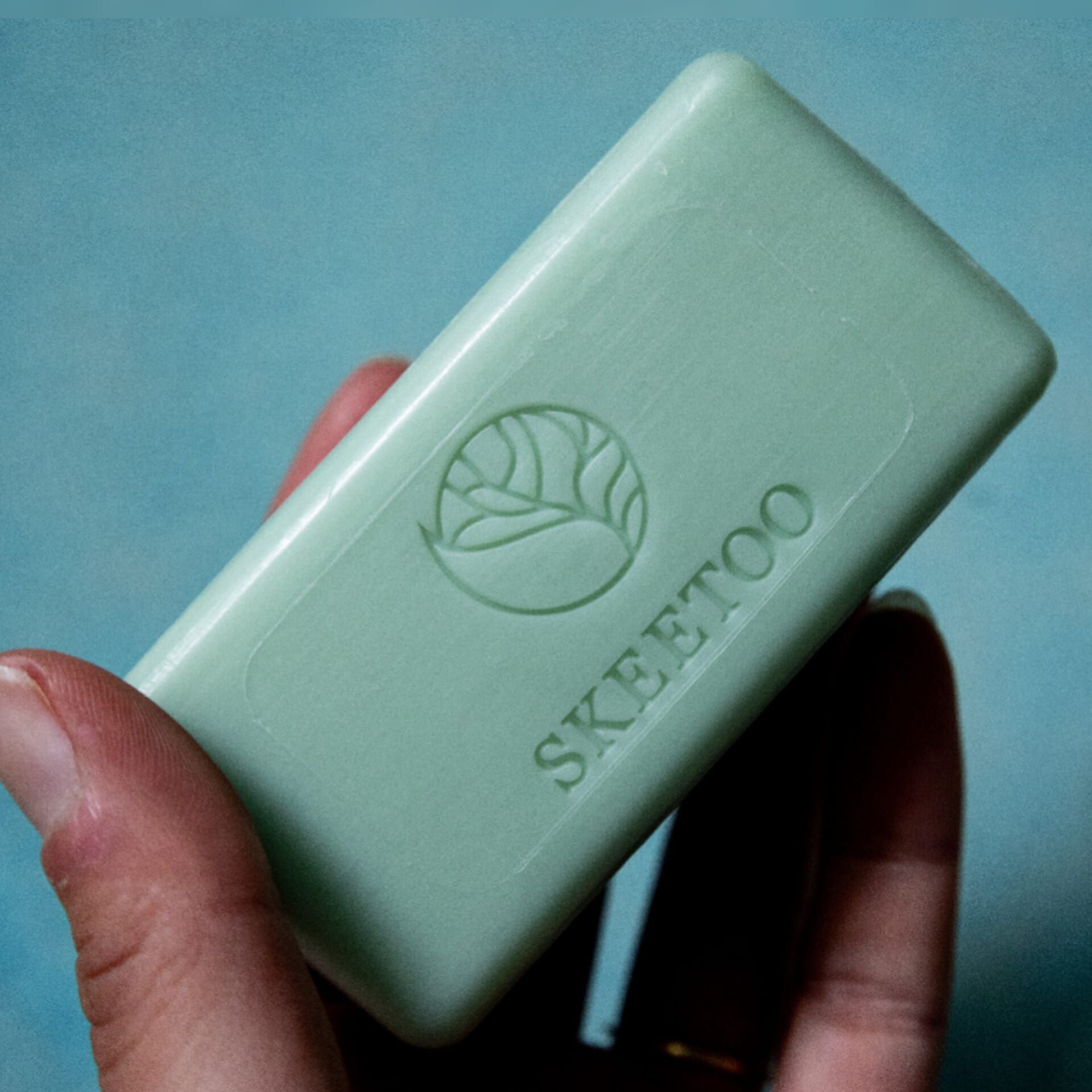 Hellgrünes Seifenstück mit Logo und Schriftzug SKEETOO. Seife wird von einer Hand gehalten.