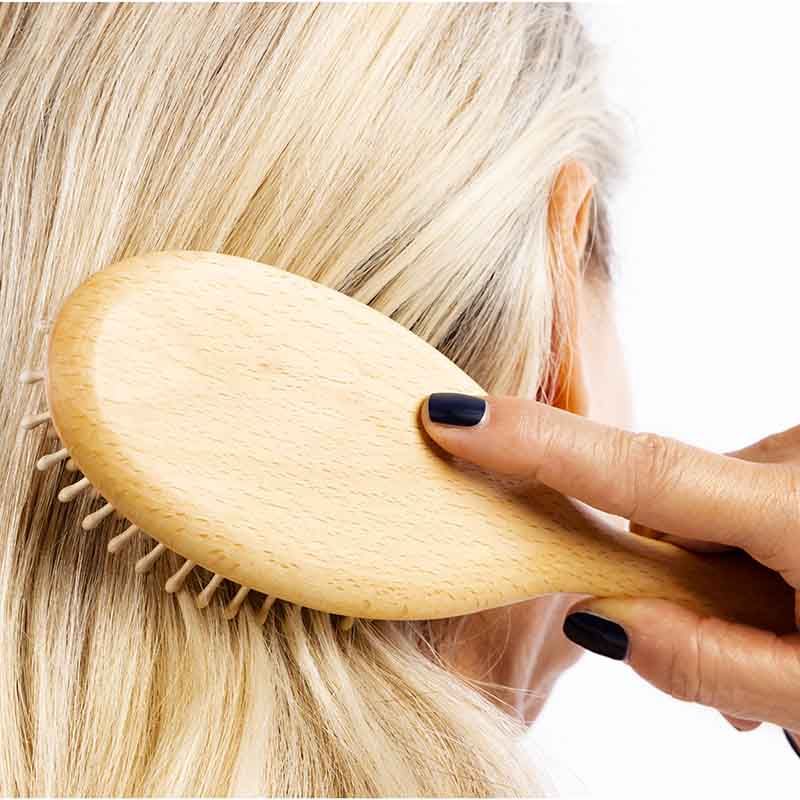 Eine Frau kämmt sich mit einer ovalen Holzbürste die Haare. Die Bürste hat helle Holzstifte. Die Frau hat graue Haare.