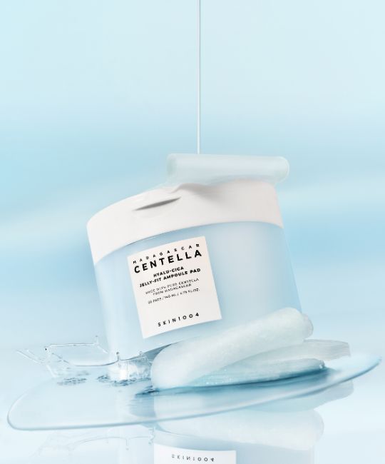 Blau-weißer Behälter, Flüssigkeit fließt heraus. Pads und Flüssigkeit auf Oberfläche. Text: CENTELLA, HYALU-CICA JELLY-FIT AMPULE PAD, SKIN1004.