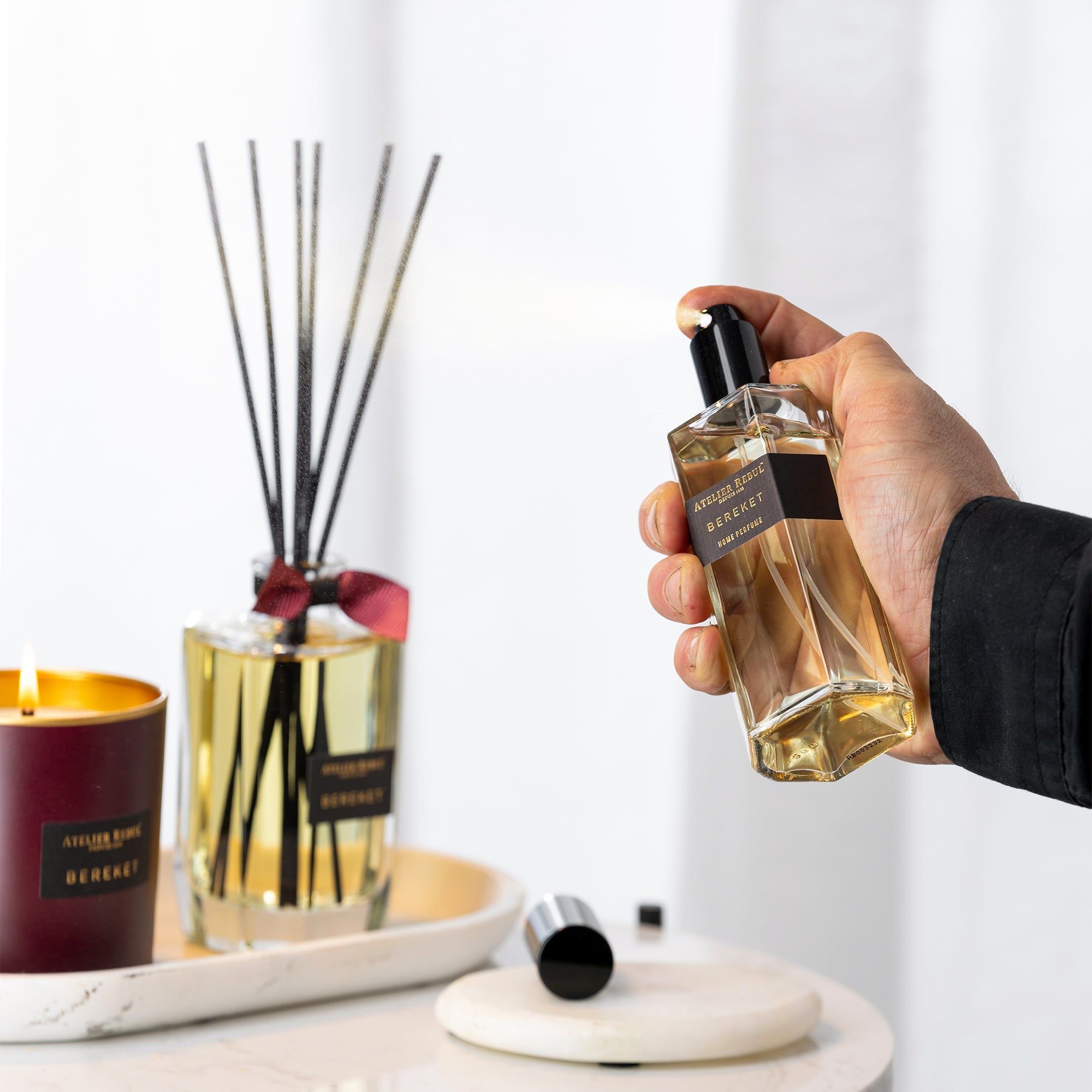 Person hält einen Flakon. Im Hintergrund Duftstäbchen, Kerze und Tablett.
