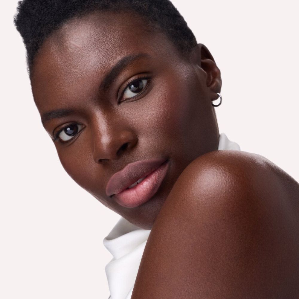 Porträt einer Frau mit dunkler Haut. Die Lippen sind mit einem rosafarbenen Lippenstift betont.