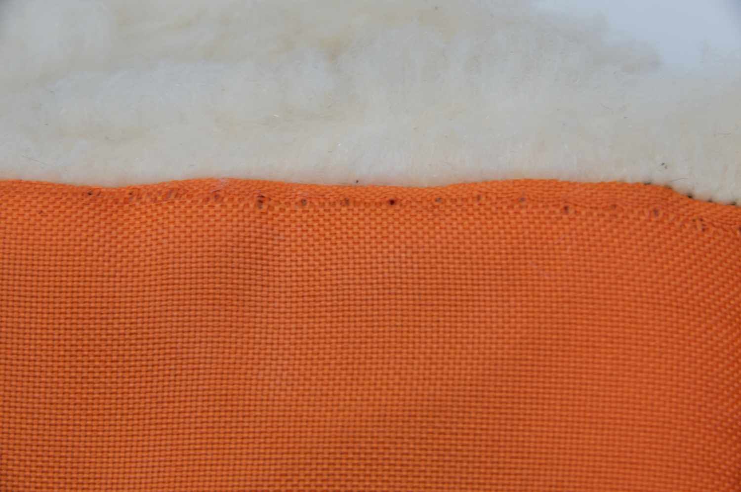 Nahaufnahme eines orangefarbenen Stoffes mit sichtbaren Nähten, verbunden mit weißem Material.