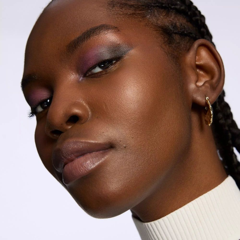 Porträt einer Frau mit dunklem Teint und violettem Lidschatten. Schwarze Haare, goldener Ohrring.