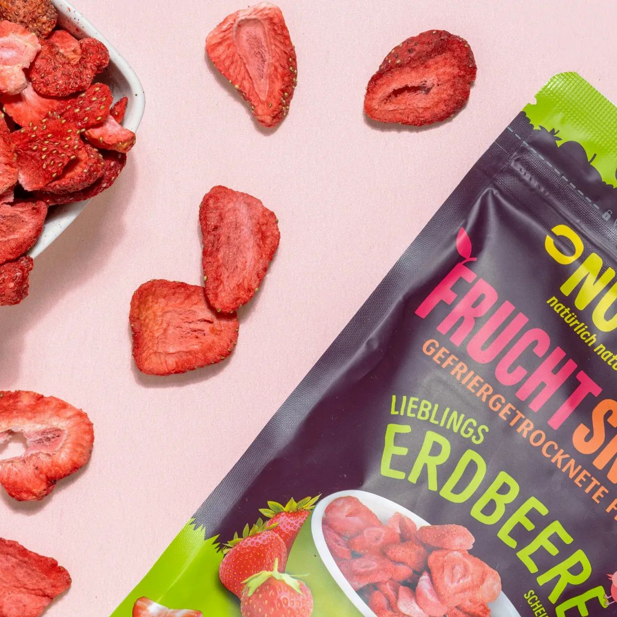 Gefriergetrocknete Erdbeeren und ein Beutel mit der Aufschrift NutriPur Fruchtsnacks Erdbeere. Erdbeeren in einer Schüssel.