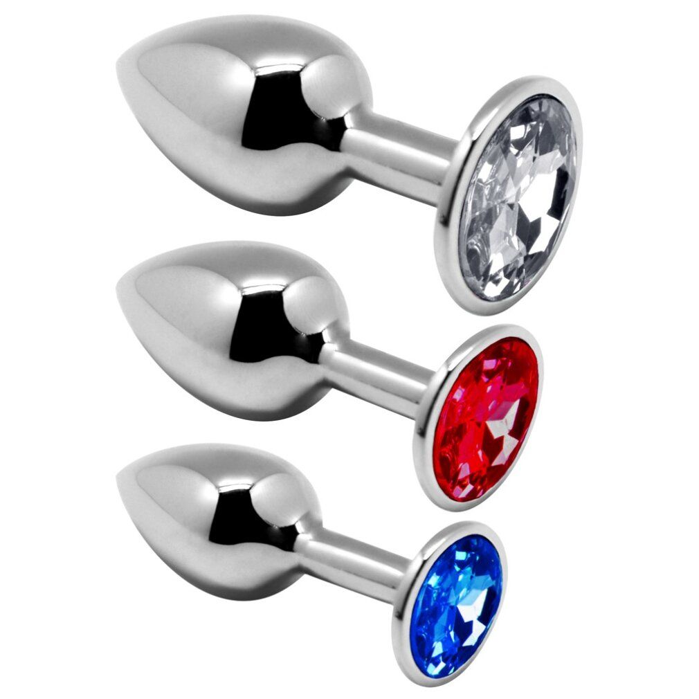 Drei metallische Anal-Plugs mit Juwelen. Einer mit klarem, einer mit rotem, einer mit blauem Stein. Glänzende Oberfläche.