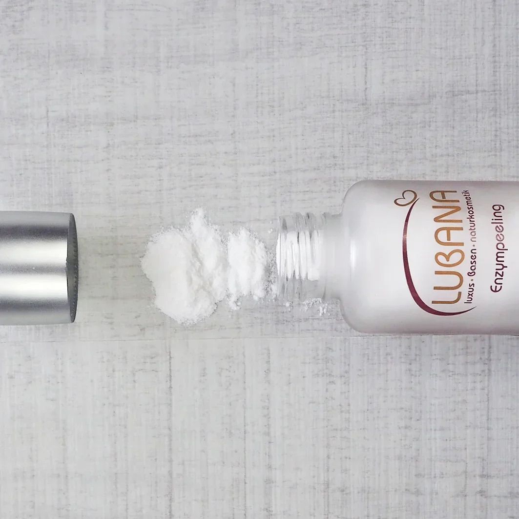 Weißes Fläschchen mit silbernem Deckel, liegend. Aufschrift: LUBANA, Enzympeeling. Daneben weißes Pulver.