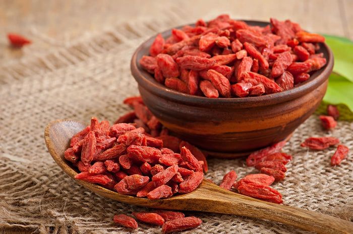 Goji Beeren in einer Schale und auf einem Holzlöffel. Rote, getrocknete Beeren auf Leinenstoff.