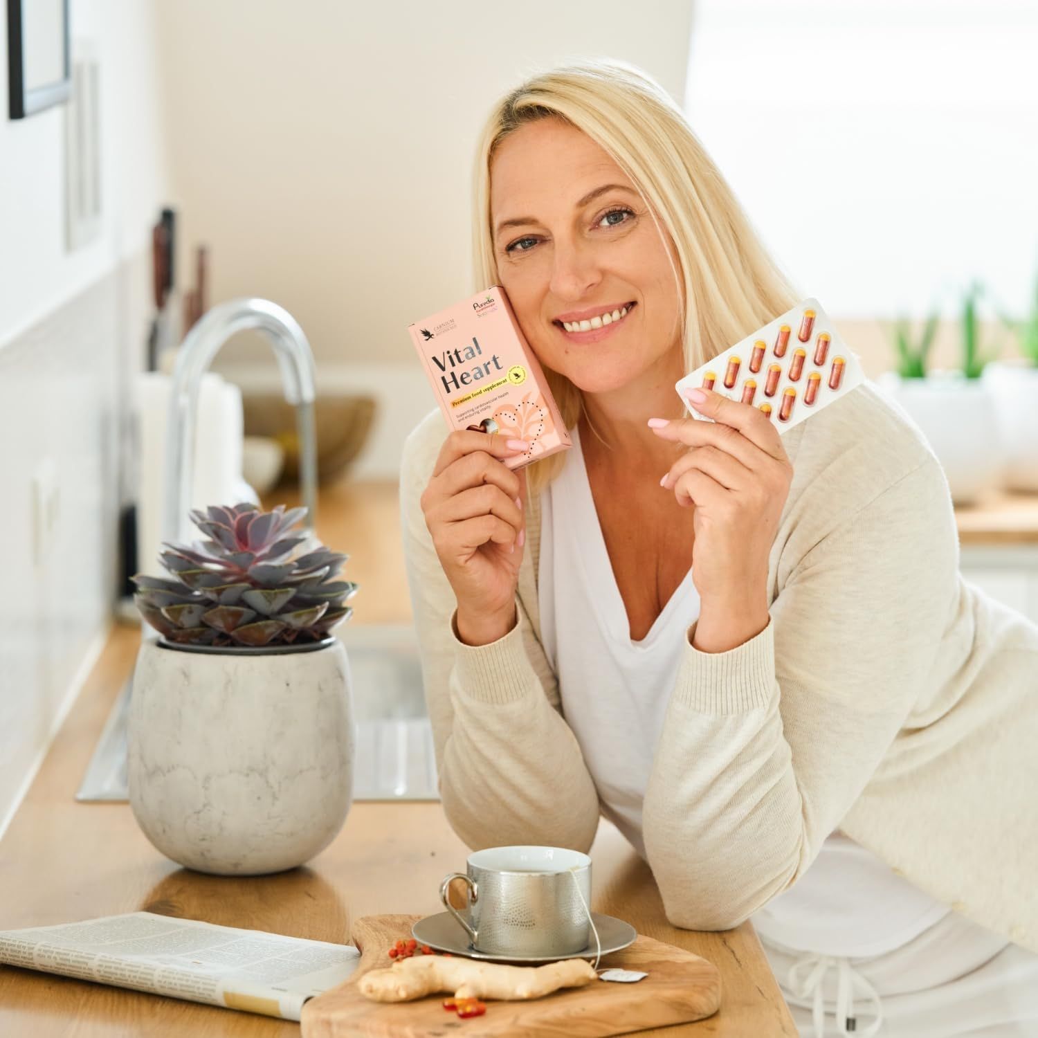 Frau hält eine rosa Schachtel "Vital Heart" und eine Blisterpackung mit Kapseln.