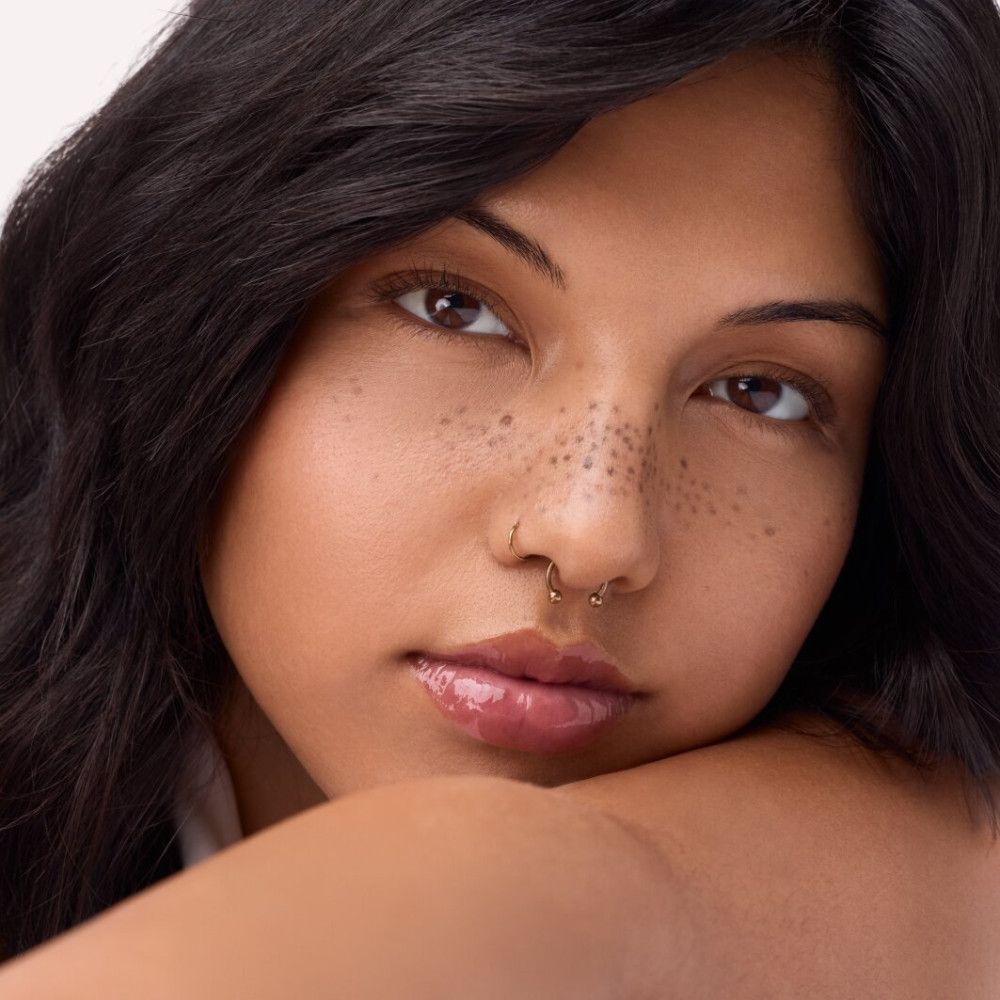 Porträt einer Frau mit Lipgloss auf den Lippen. Hautton, dunkle Haare, Nasenpiercing.