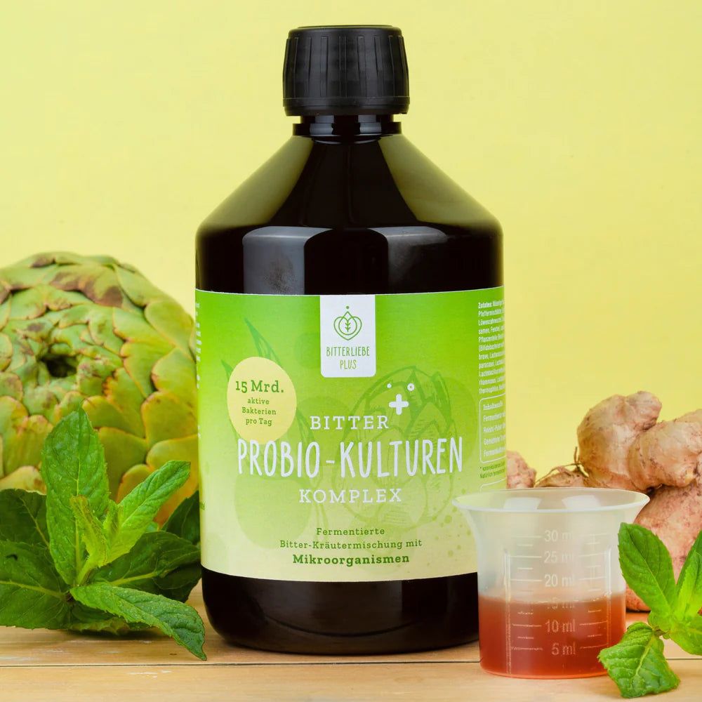 Braune Flüssigkeit in einer Flasche, daneben ein Messbecher mit Flüssigkeit. Aufschrift: BitterLiebe Probio Kulturen Komplex.