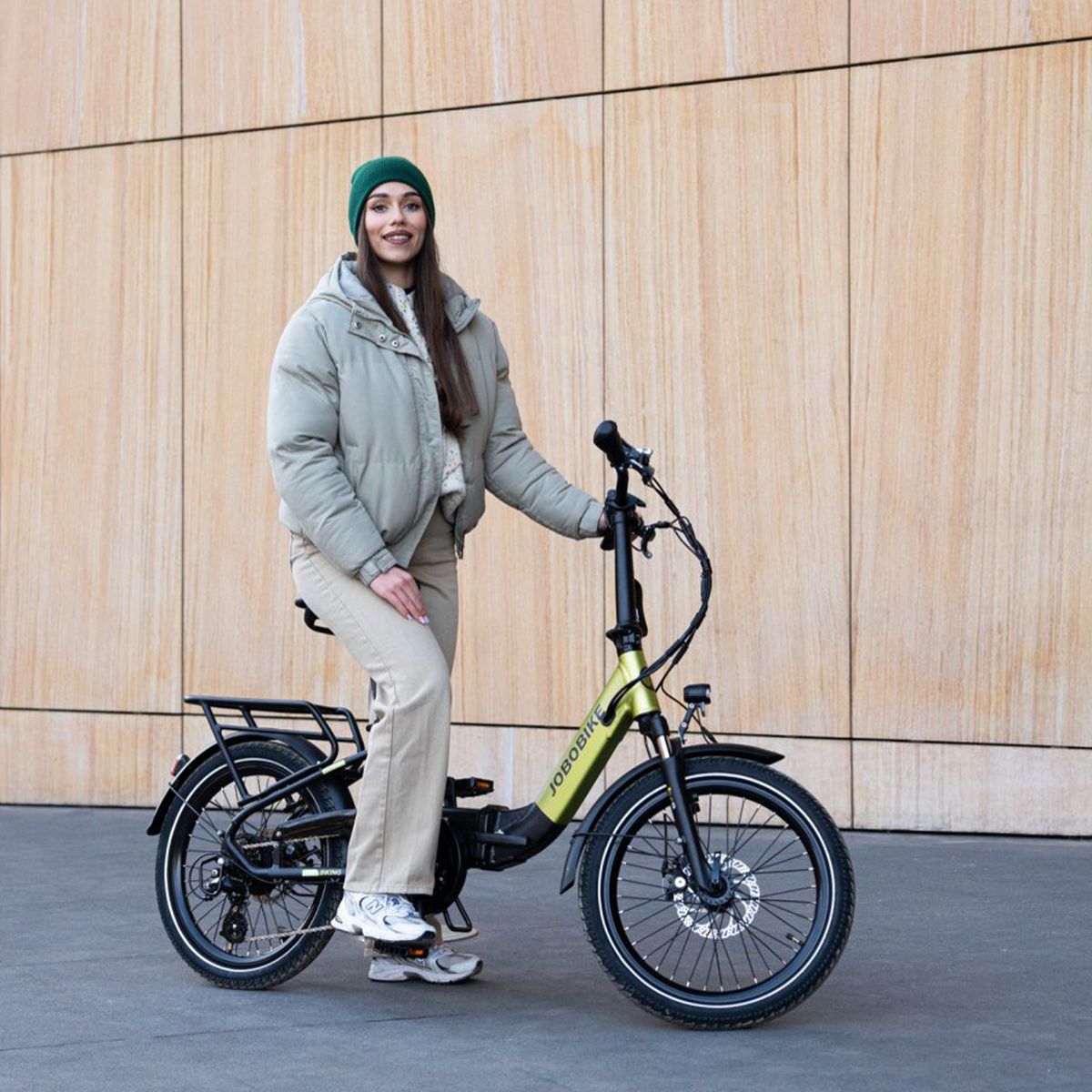 Faltbares E-Bike, grün-schwarz, mit Person. JOBOBIKE-Logo. Gepäckträger, Schutzbleche. Person trägt Winterkleidung.