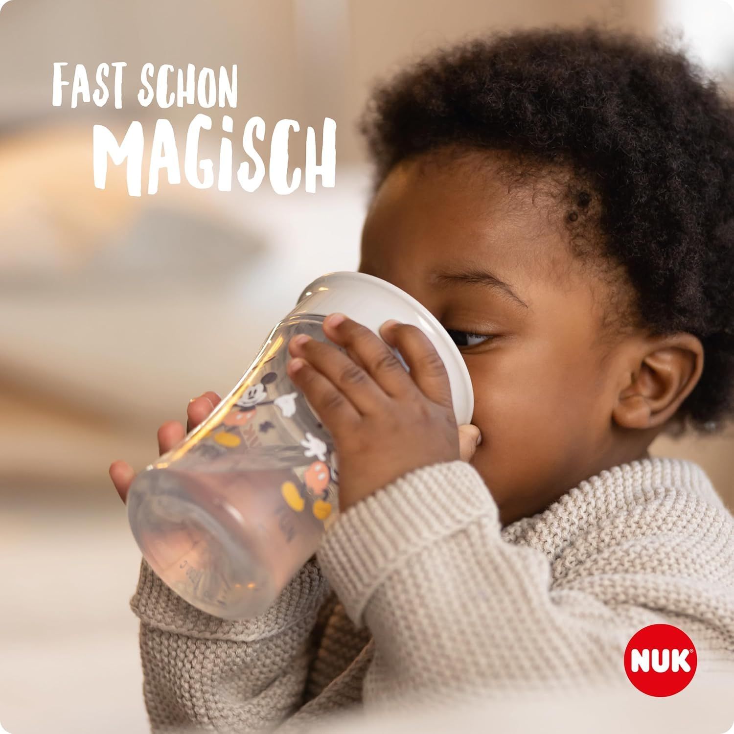 Kind trinkt aus einem Trinkbecher. Becher mit Mickey Mouse-Motiv. NUK Logo.