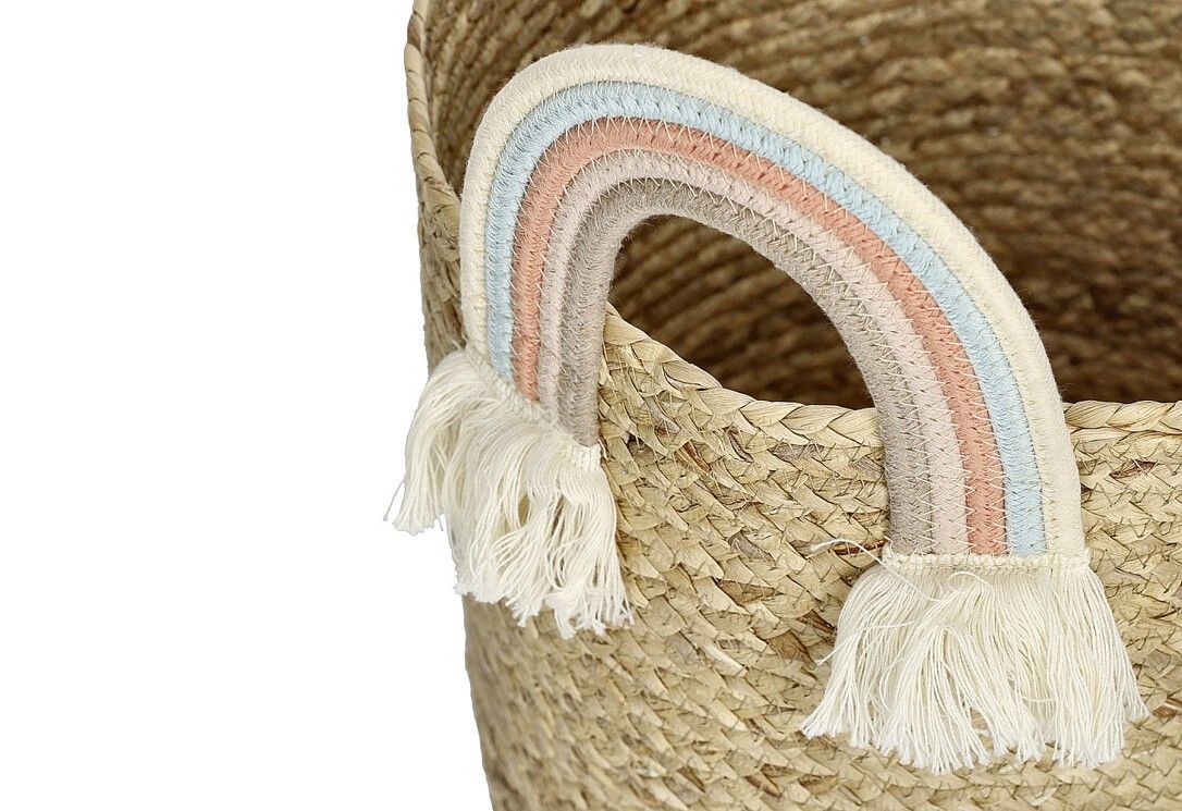 Nahaufnahme eines runden Aufbewahrungskorbs mit Regenbogen-Henkel. Fransen an den Henkeln. Korb aus Naturmaterial.