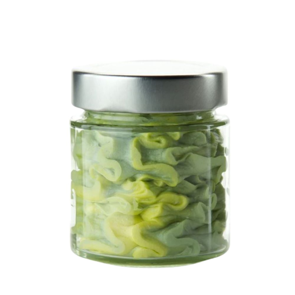 Glasbehälter mit grün-gelben, wellenförmigen Inhalten und silbernem Deckel. Auf weißem Hintergrund.