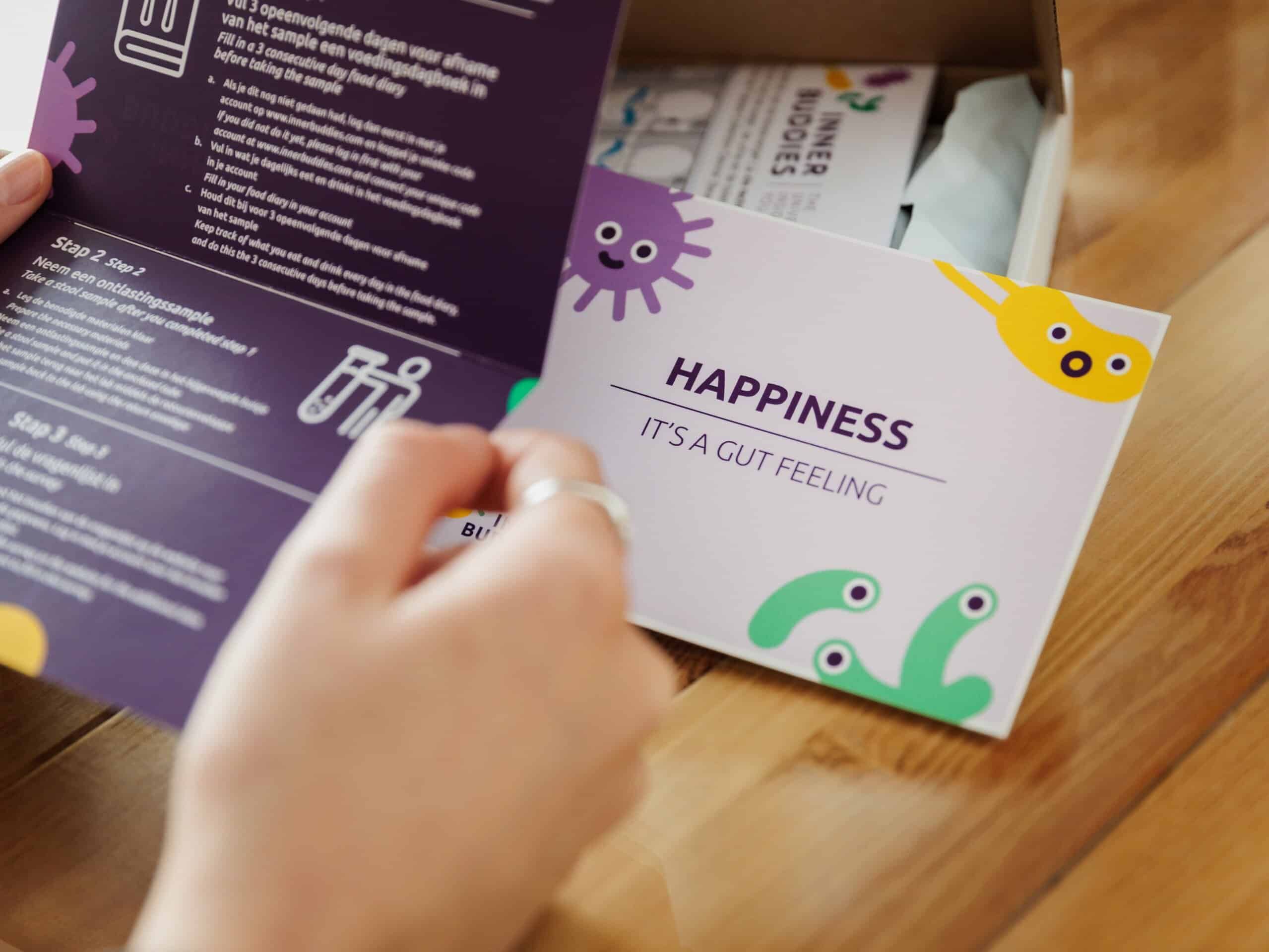 Person hält eine Broschüre mit Mikroben-Illustrationen und dem Text „HAPPINESS IT'S A GUT FEELING“.