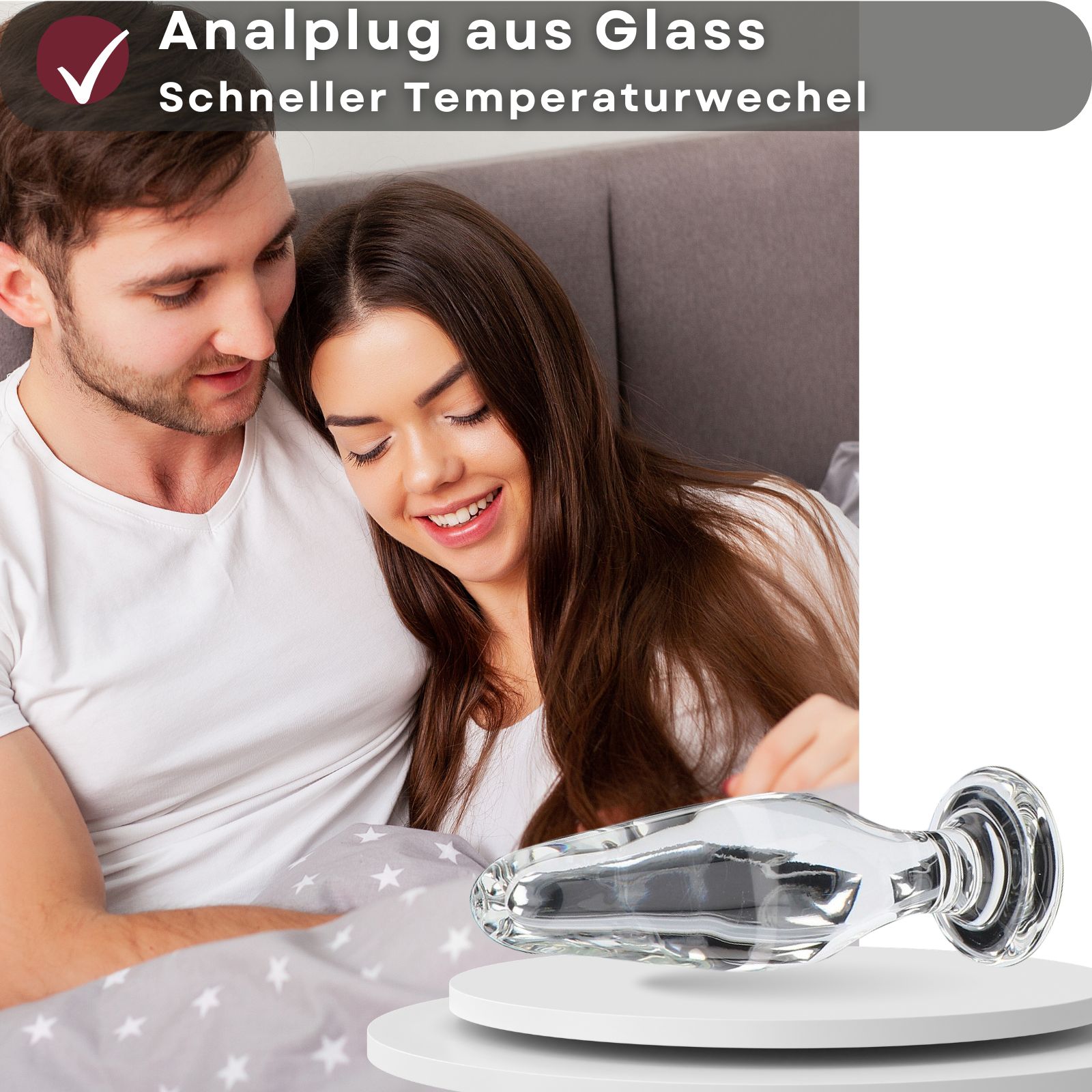 Analplug aus Glas. Transparentes Material. Auf weißem Podest. Paar im Hintergrund. Auf hellem Hintergrund.