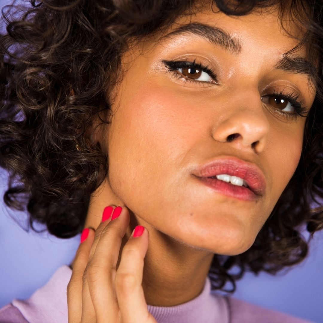 Nahaufnahme einer Frau mit Make-up. Sie berührt ihren Hals. Sichtbar sind Lippenstift und Nagellack.