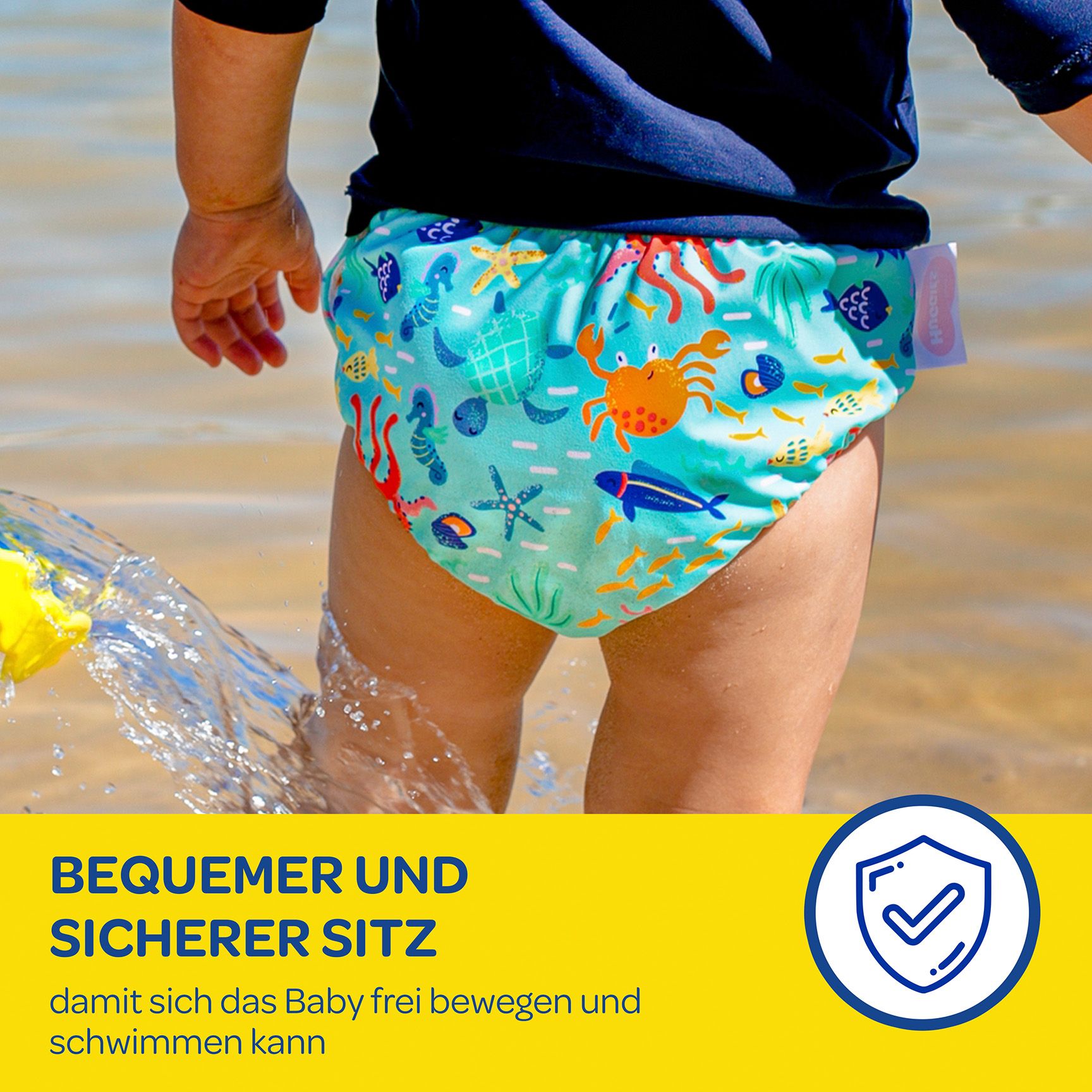 Kind im Wasser trägt Schwimmwindel mit Meeresmotiven. Text: Bequemer und sicherer Sitz.